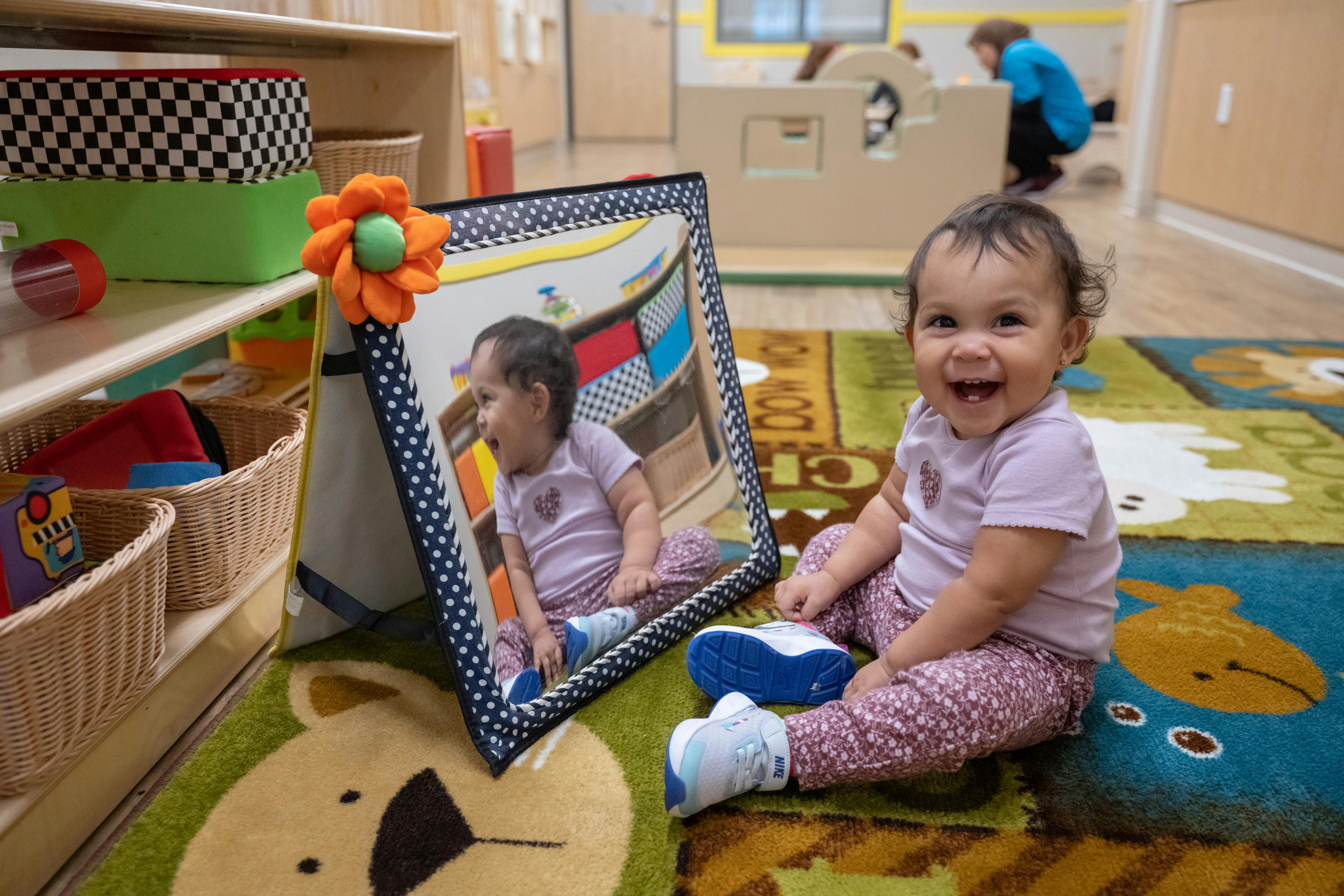 Child sitting on a rug next to a mirror, looking forward