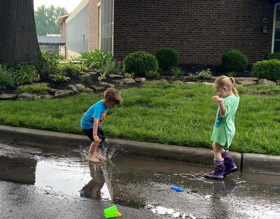 Child splashing in a puddle while another child watches