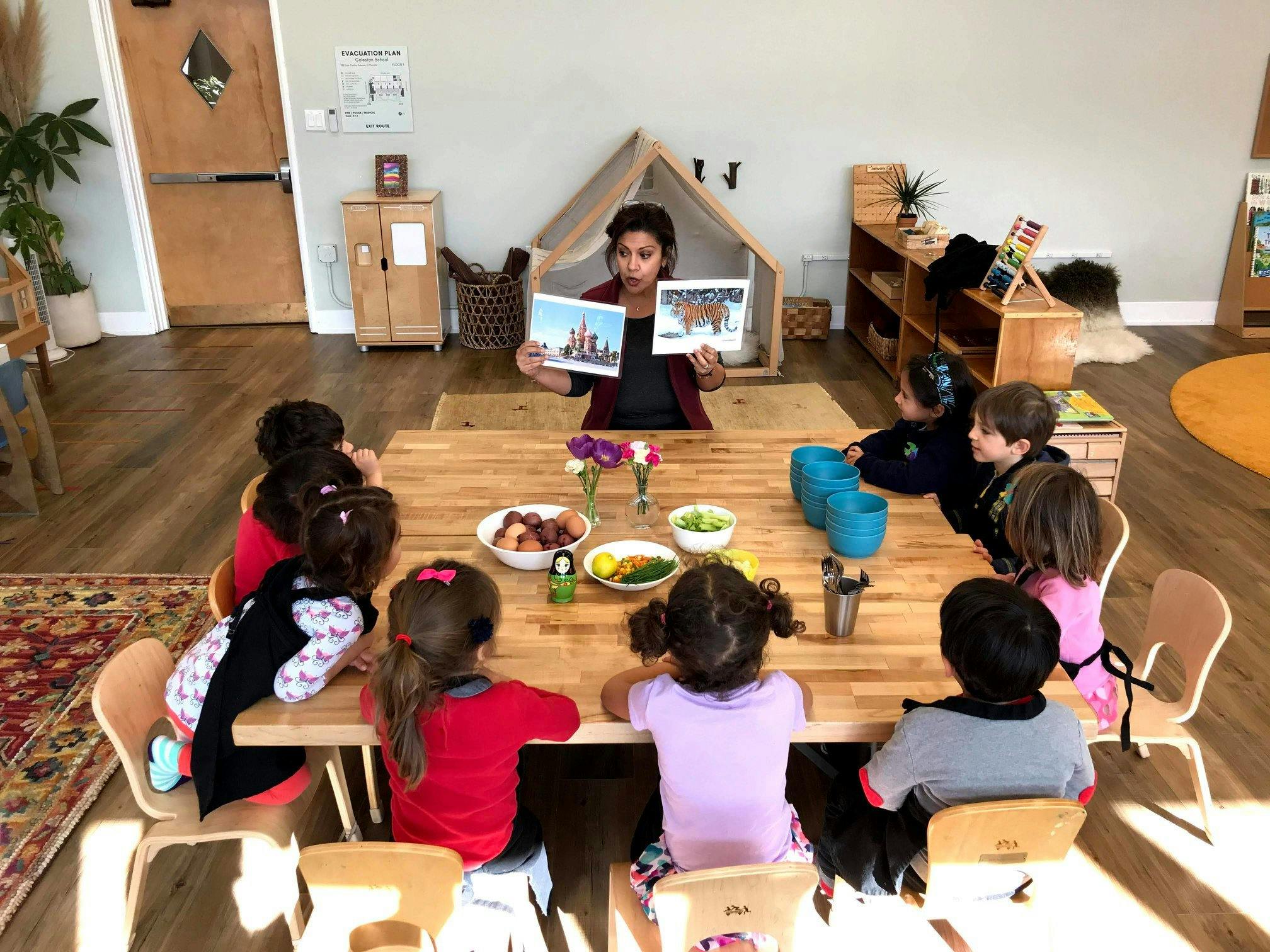 Person reading a book to children seated around a table in a classroom