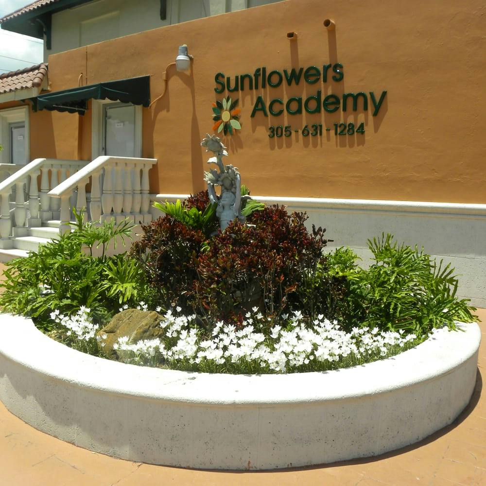 Planter with flowers and shrubs in front of a building with "Sunflowers Academy" sign
