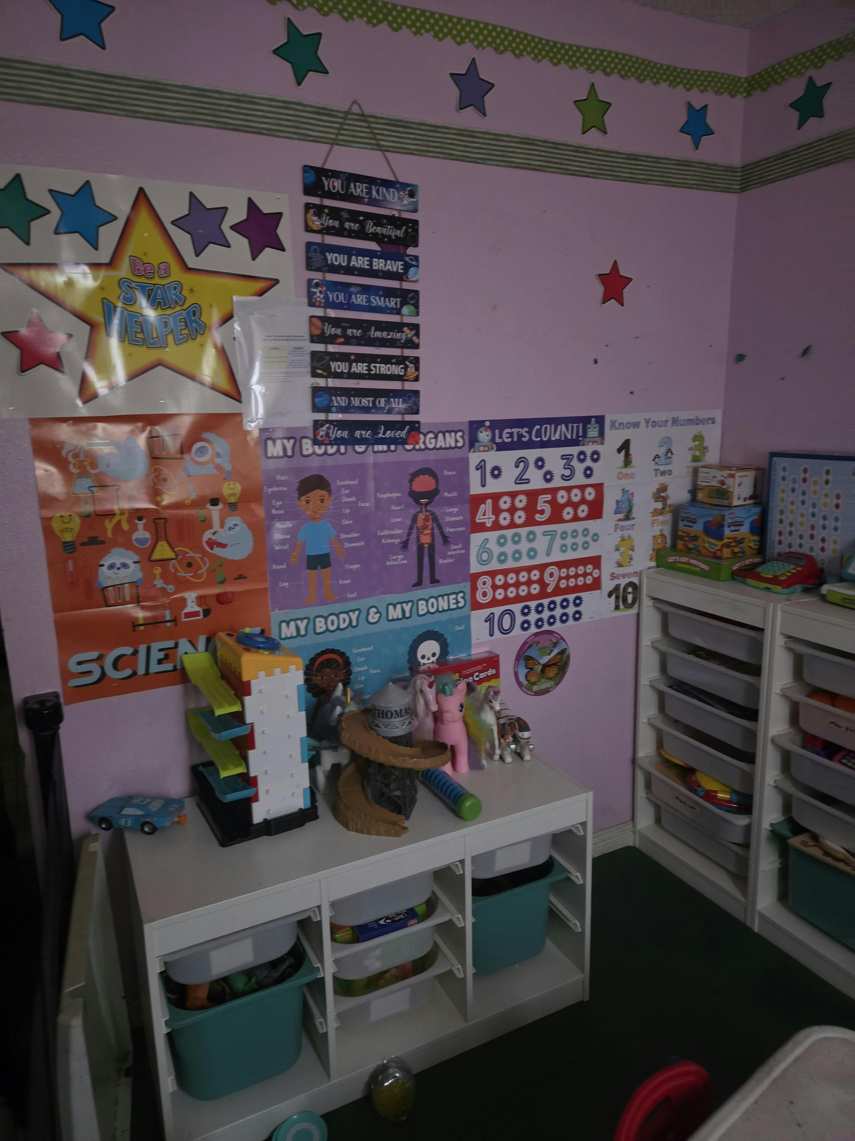 Classroom wall decorated with educational posters and stars, storage shelves with toys