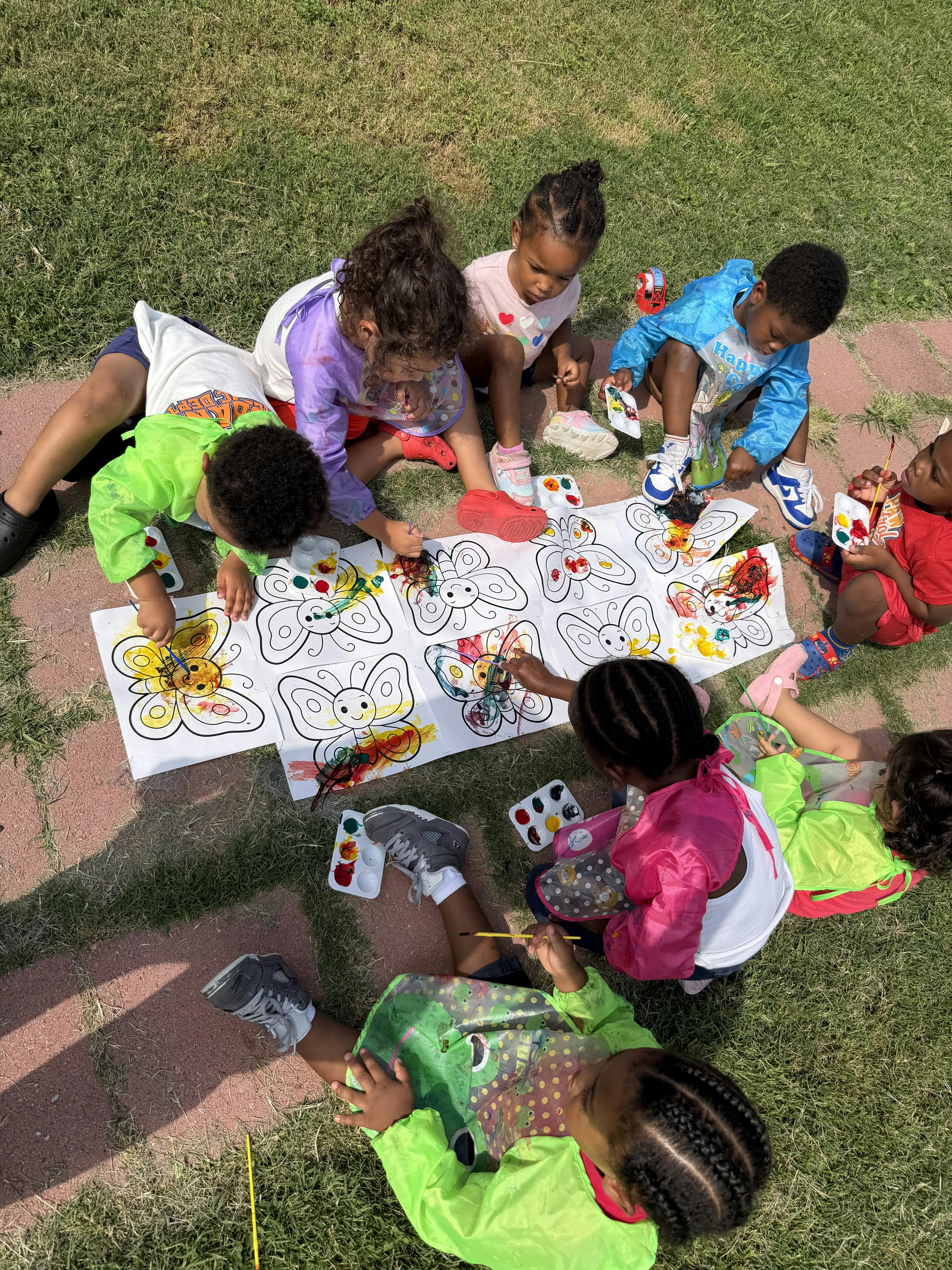 Group of children painting butterfly illustrations on paper outdoors on the grass