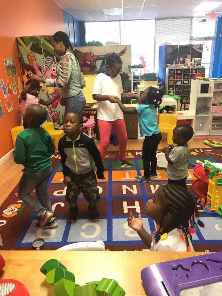 Adults and children standing on an alphabet rug in a classroom