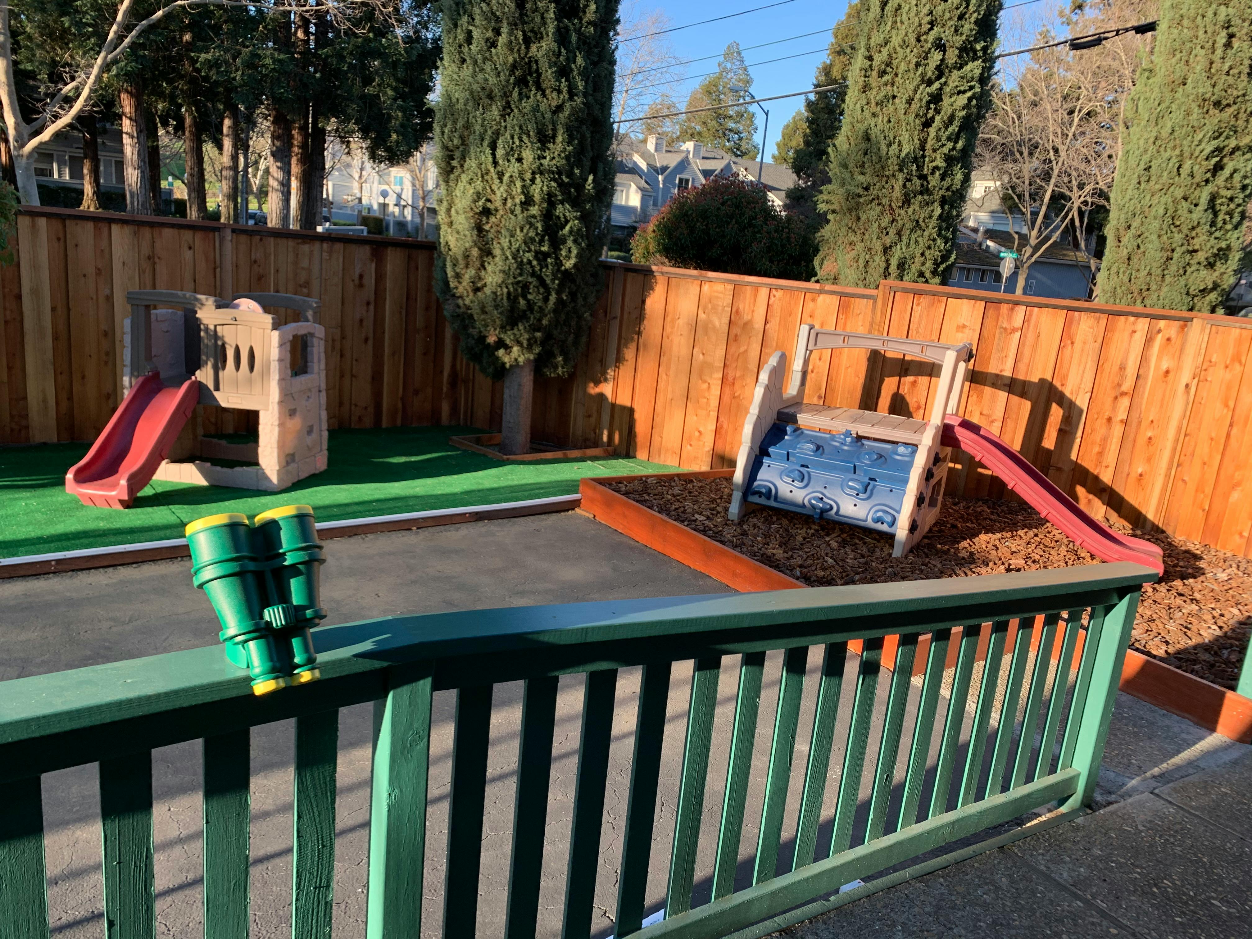Binoculars on a green railing overlooking a playground with slides