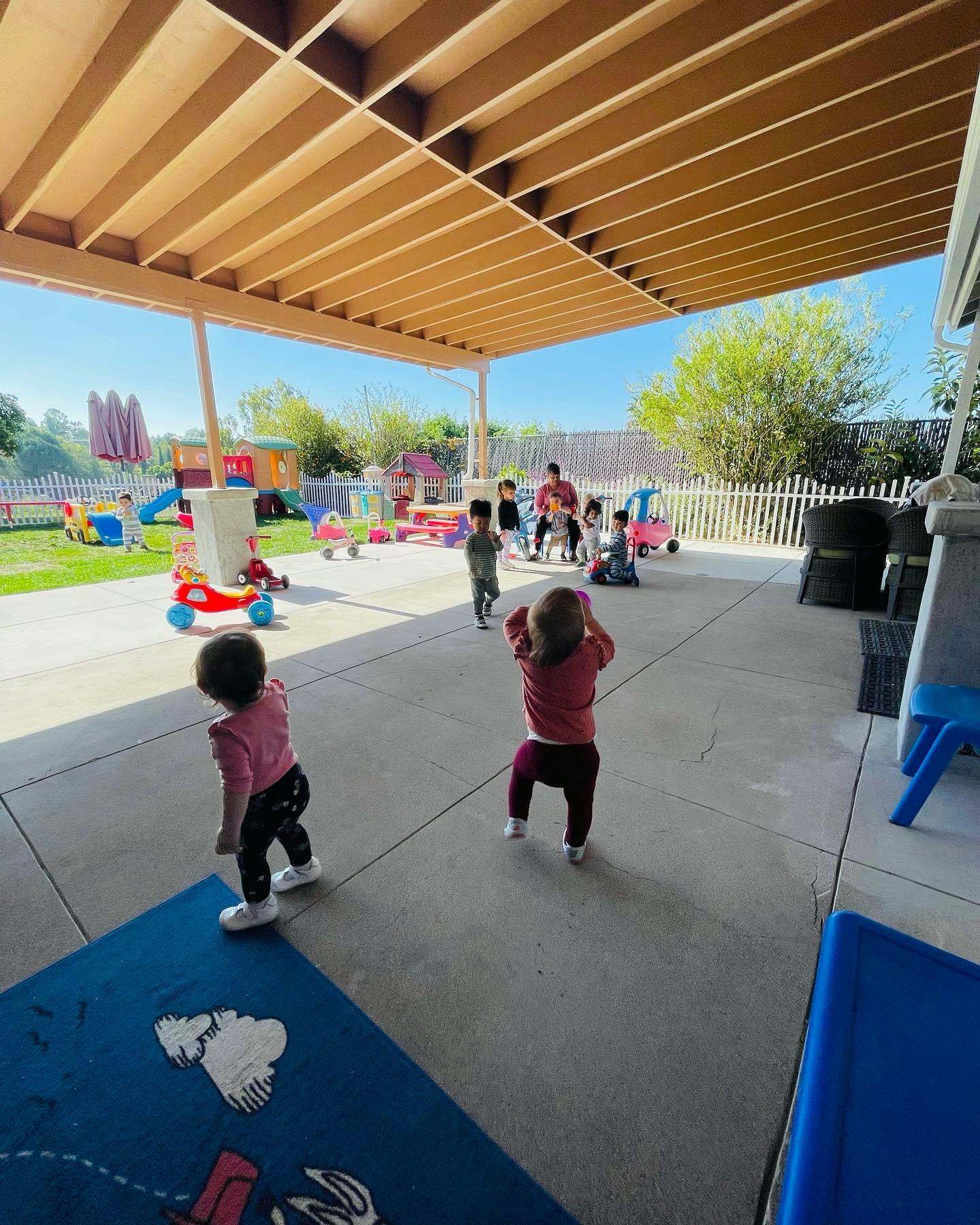 Children playing on a covered patio with a playground in the background