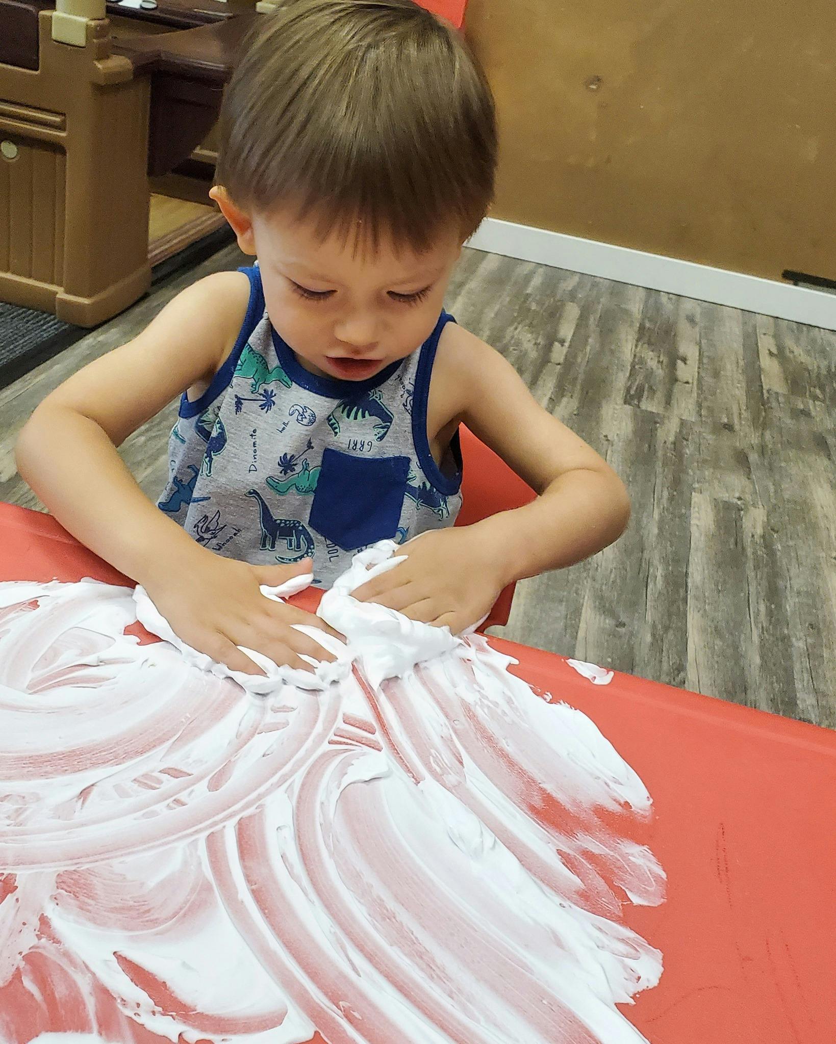 Child playing with shaving cream on a red surface