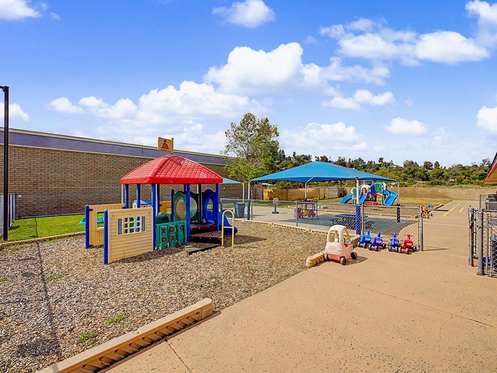 Childcare playground with play structures, shade, and small ride-on toys