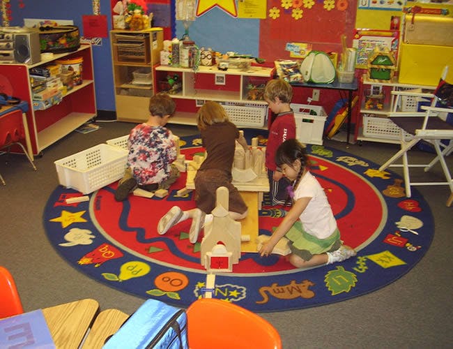 Children playing with toys on a colorful rug in a classroom