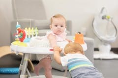 Child in a baby walker with another child standing nearby
