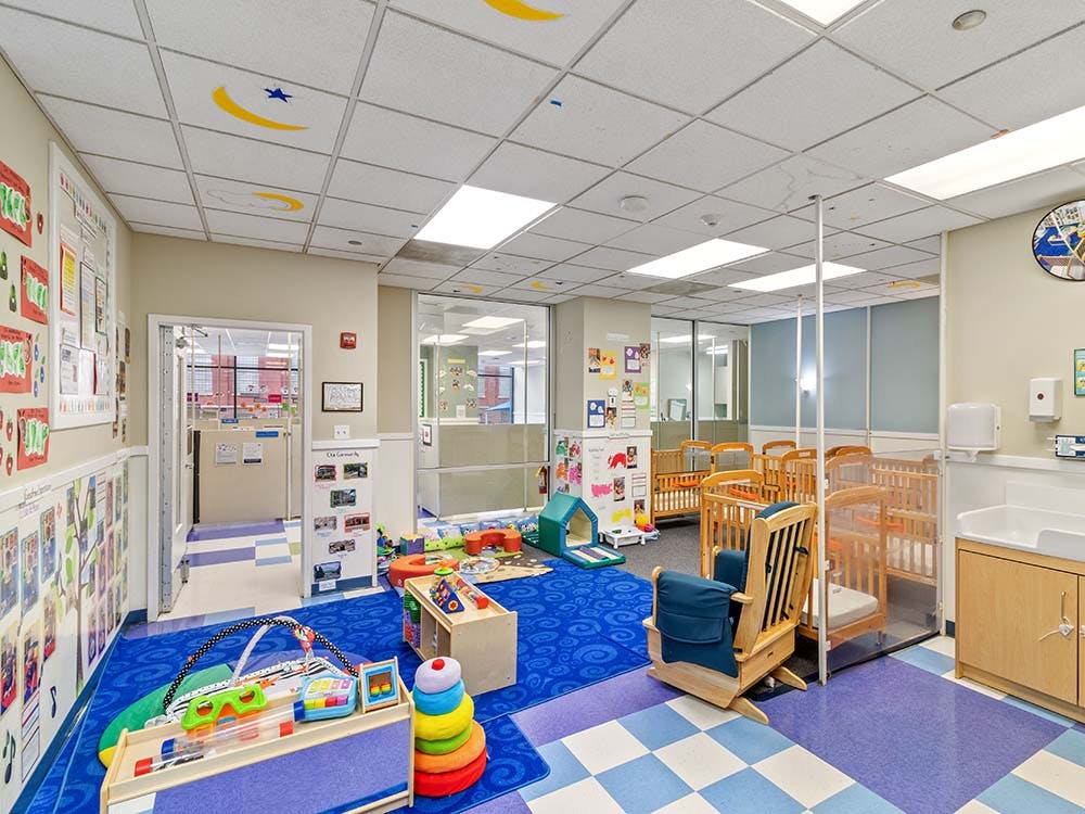 A colorful daycare room with cribs, playmats, and toys
