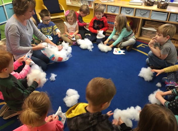Adult and children sitting in a circle on a blue rug with cotton balls