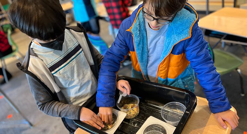 Two children working with containers of seeds or grains in a classroom