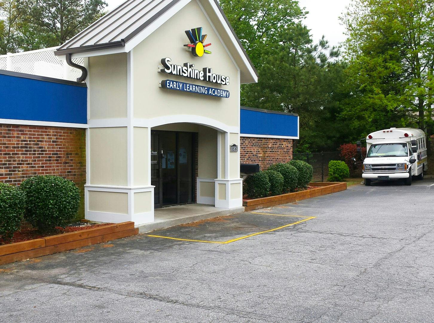 Building with "Sunshine House Early Learning Academy" sign and a white bus