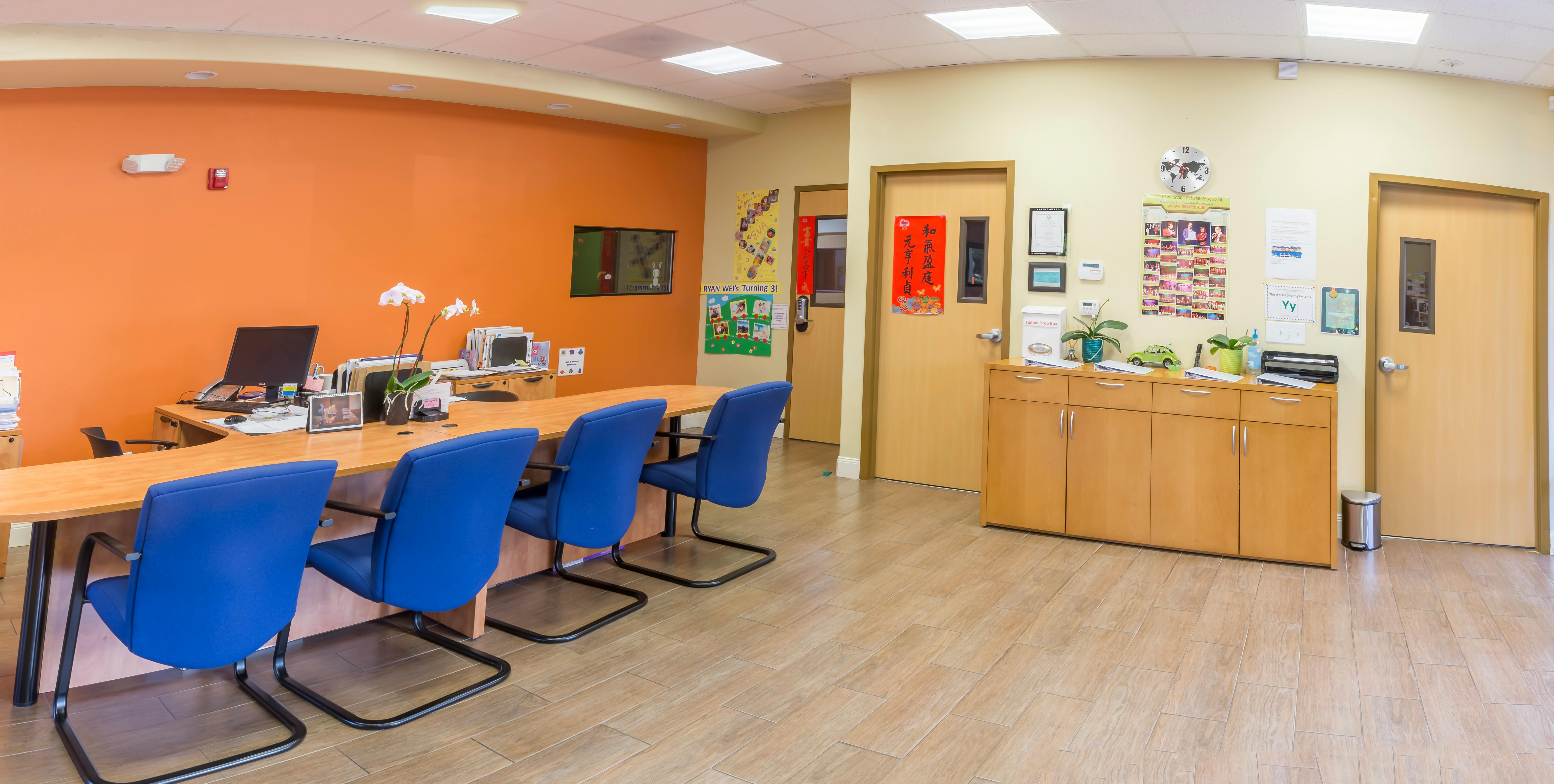 Reception area with a long desk and blue chairs against an orange wall