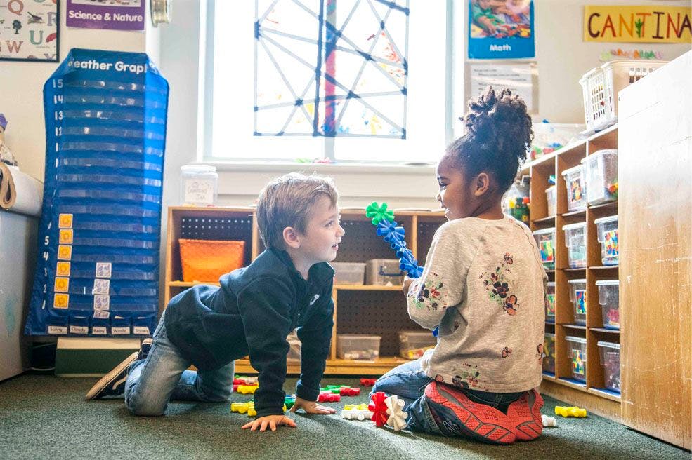 Two children playing with toys on the floor in a classroom