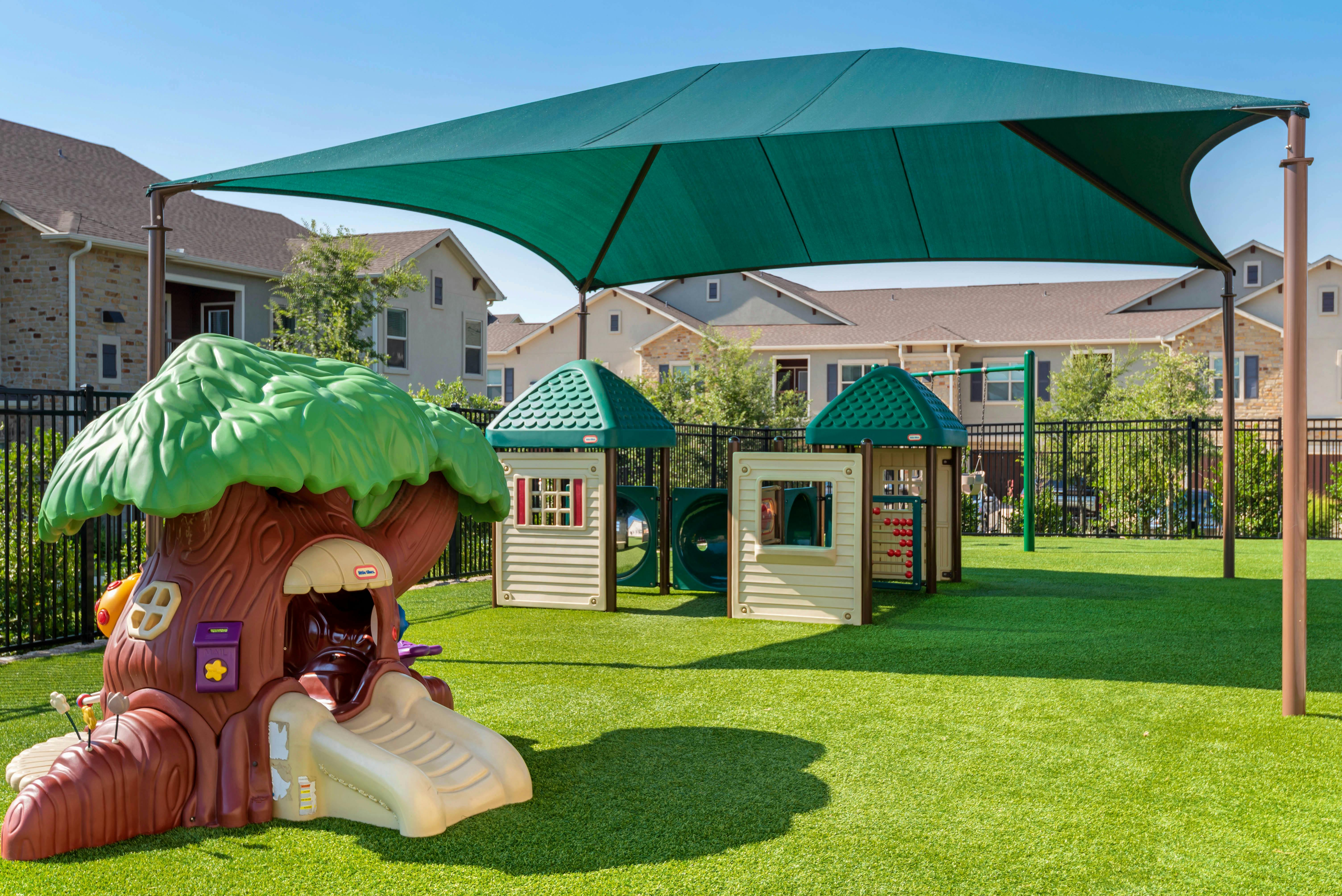 Playground with treehouse slide, small playhouses, swings, and shade canopy