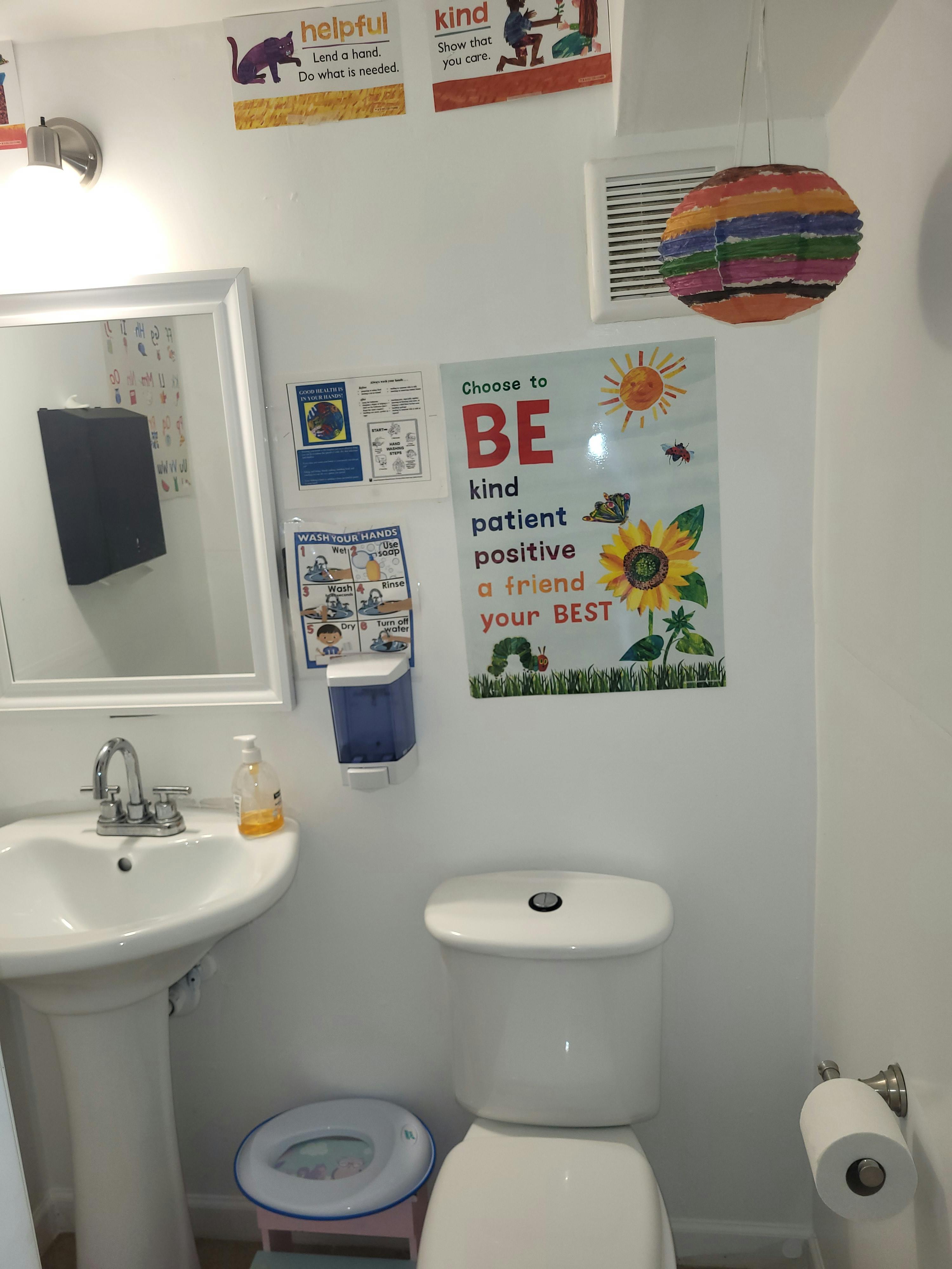 Small children's bathroom with toilet, sink, mirror, and colorful posters