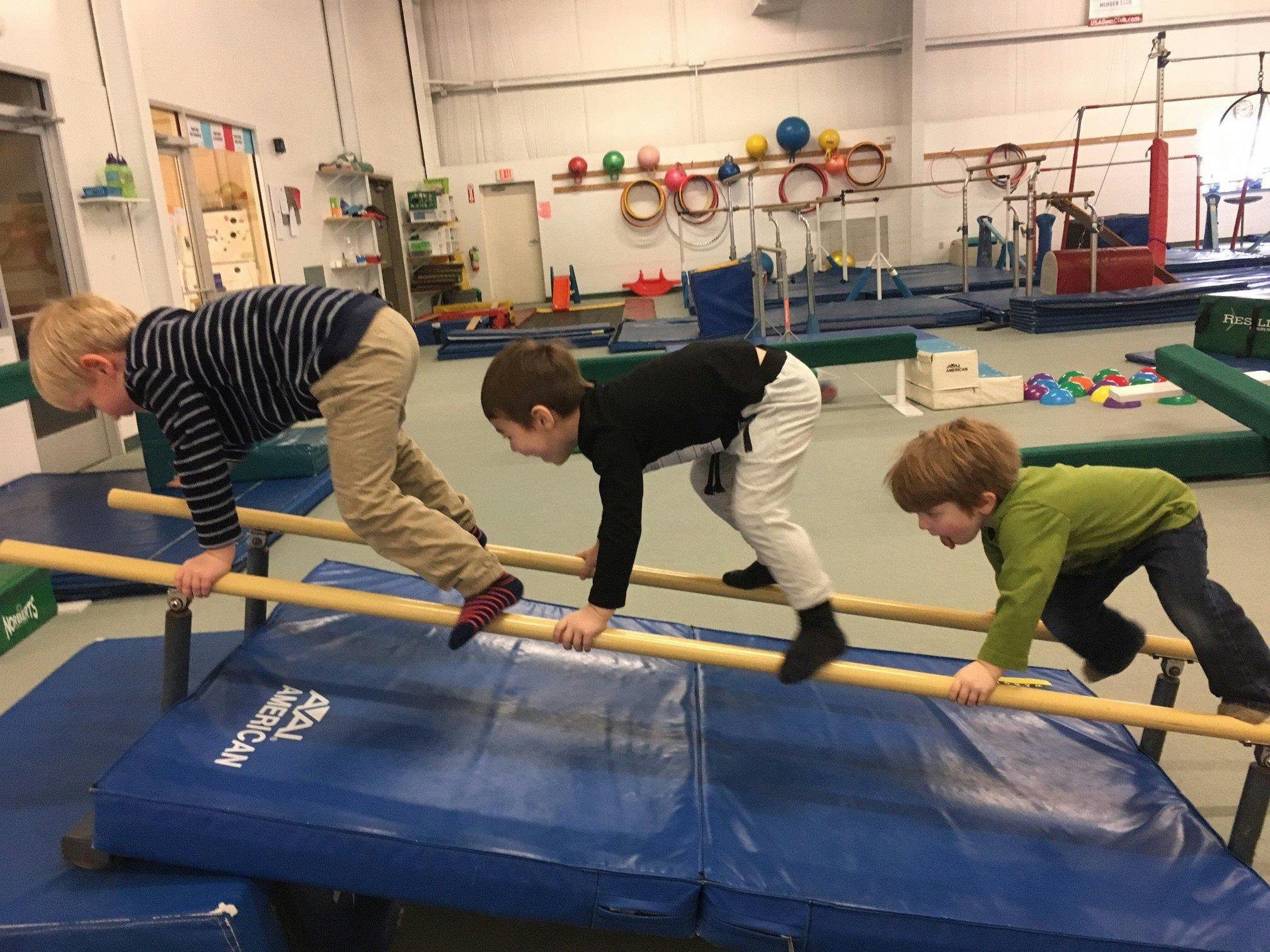 Three children crawling on parallel bars in a gym