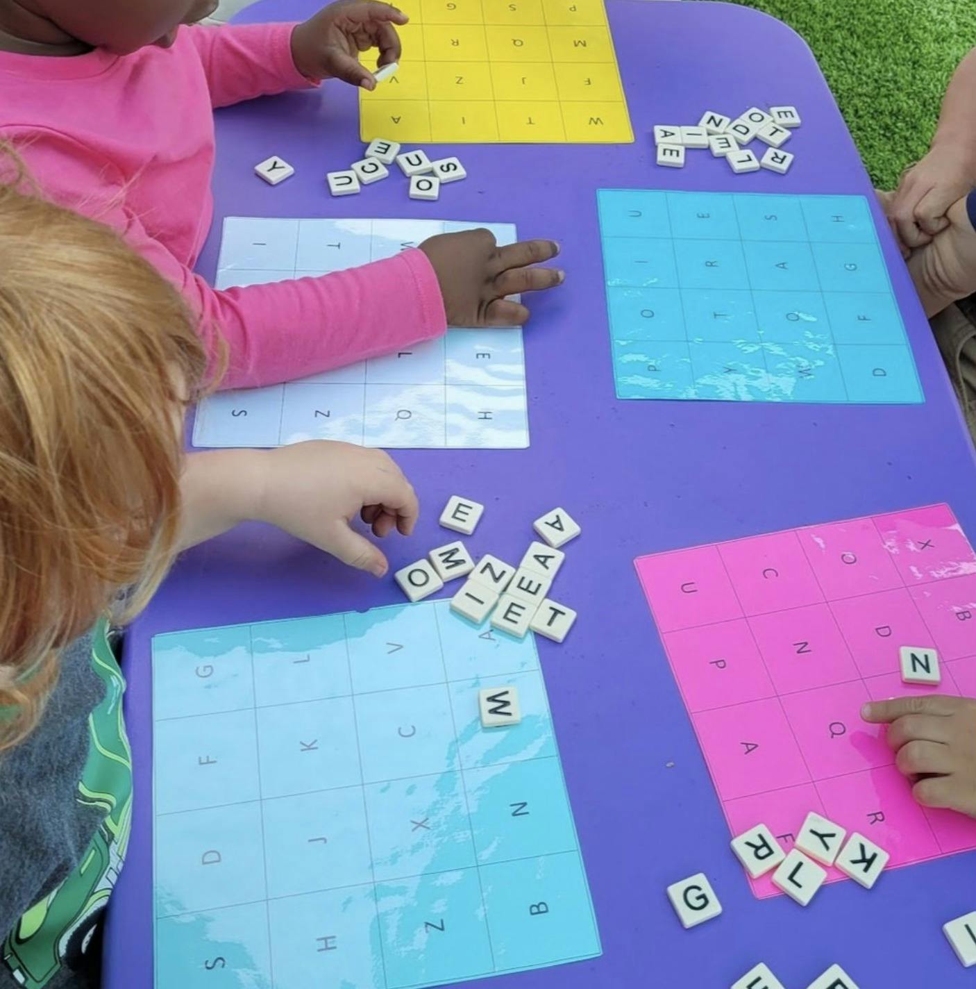 Children playing with letter tiles on a purple table with colorful mats