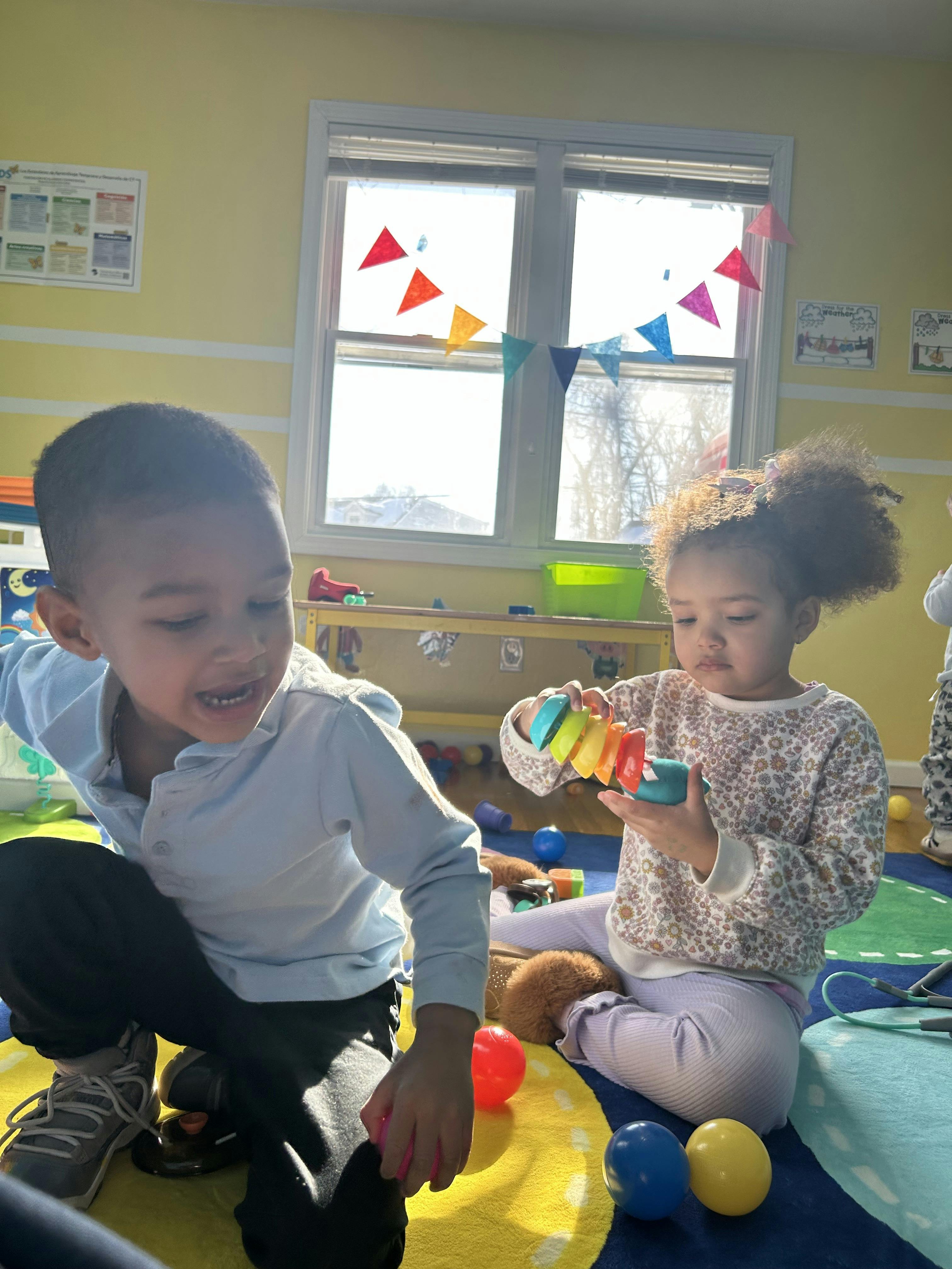 Two children playing on a colorful rug in a classroom