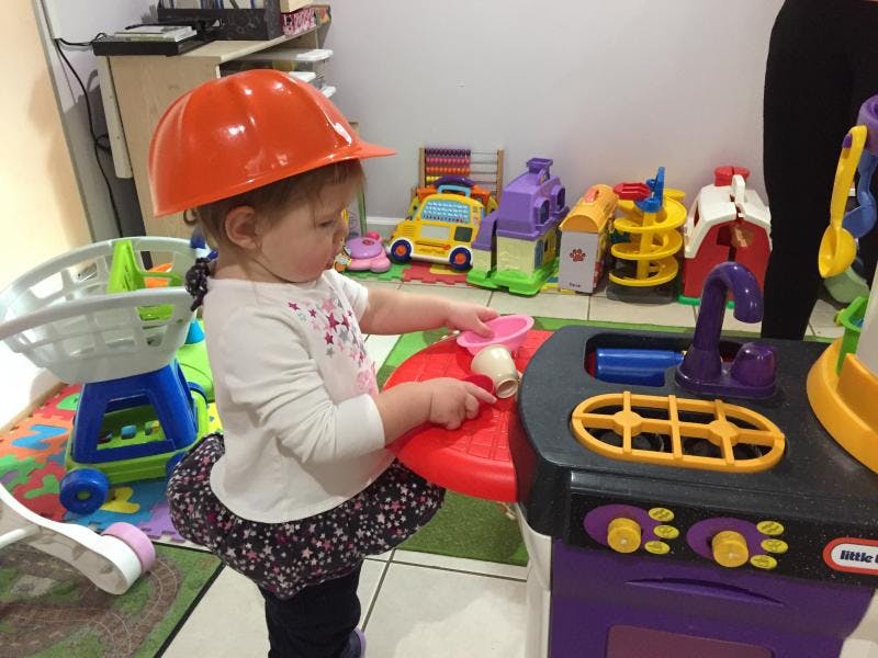 Child wearing an orange hard hat playing with a toy kitchen set
