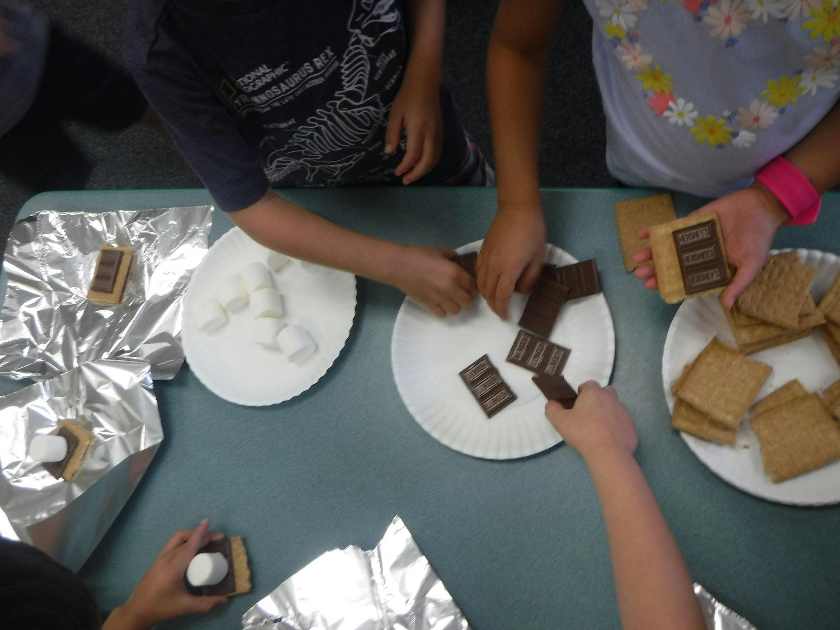 People assembling s'mores with graham crackers, chocolate, and marshmallows
