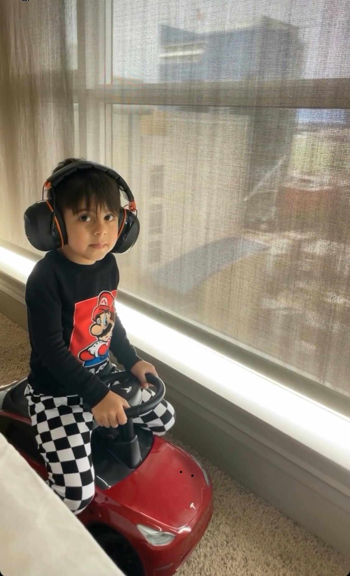 Child wearing headphones and a Mario shirt, sitting in a toy car