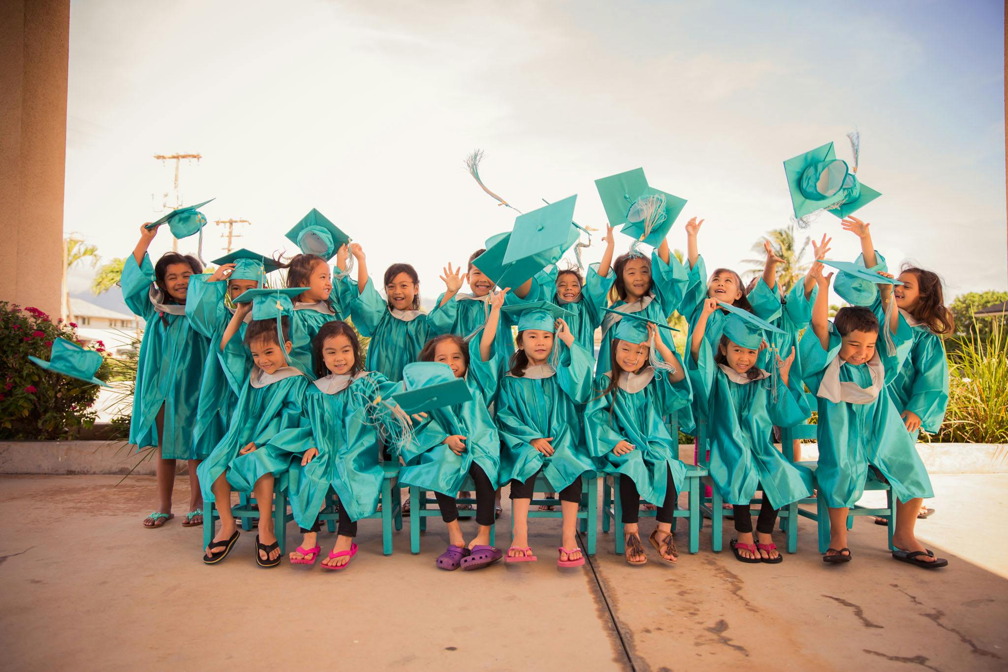 Group of children in teal graduation gowns throwing caps in the air