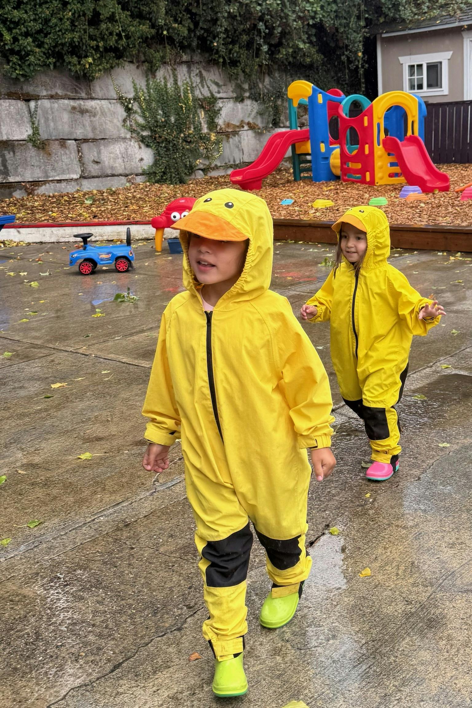Two children wearing yellow duck rain suits playing in a playground