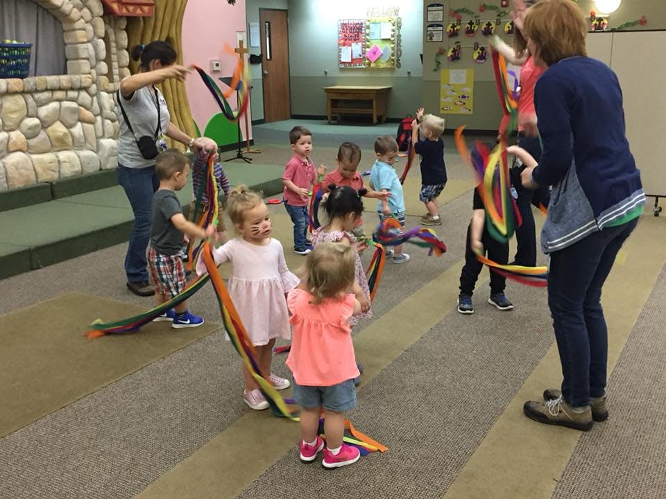 Adults and children holding colorful ribbons in a room