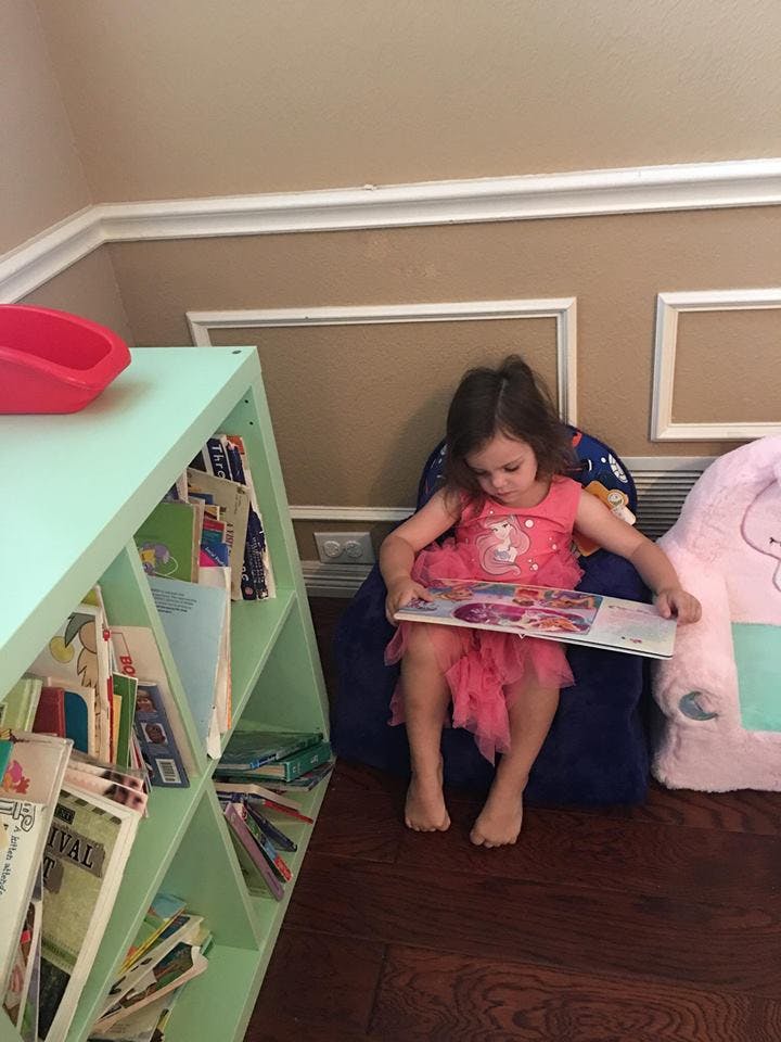 Child in a pink dress sitting in a chair and reading a book