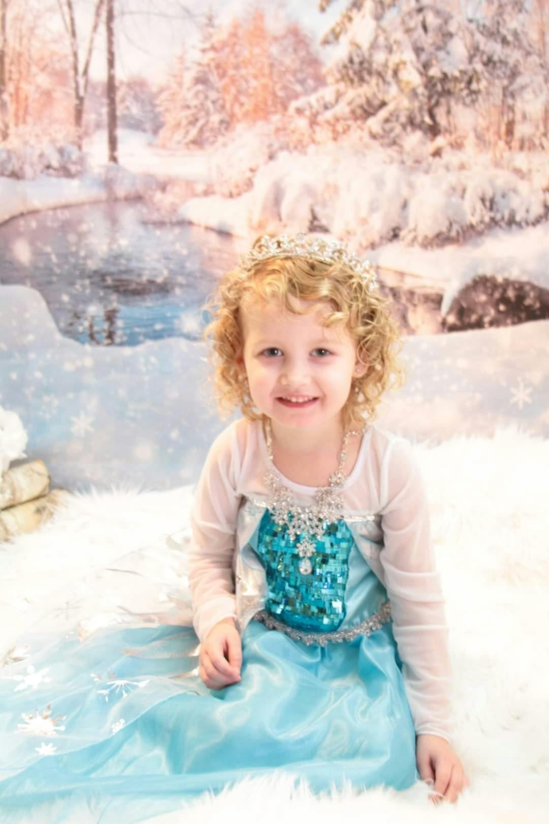 Child in a blue dress and crown sitting in a snowy setting