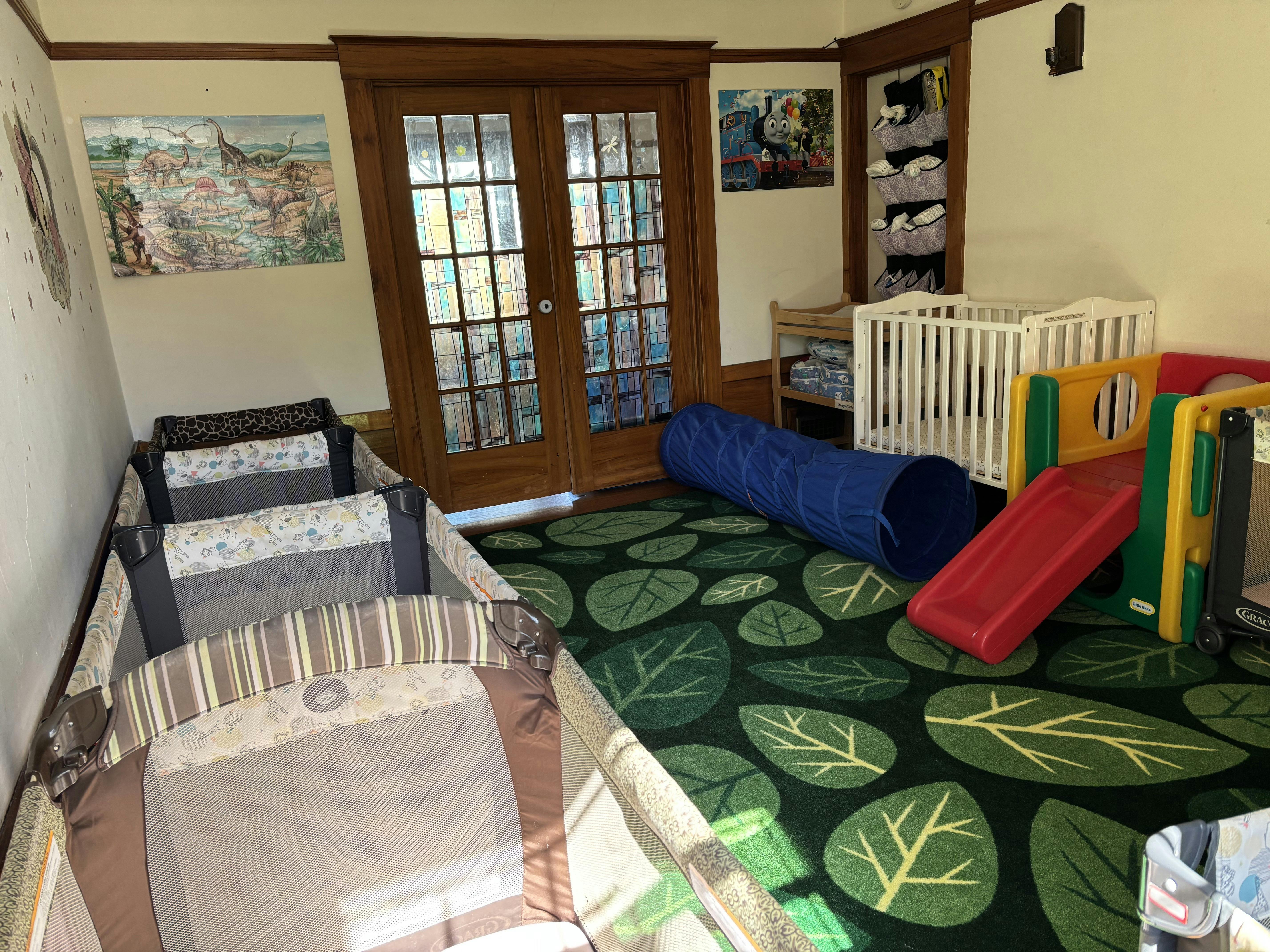 Childcare room with multiple playpens a small slide and a floor tunnel