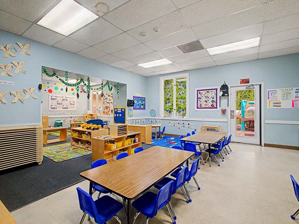 Classroom with tables, blue chairs, shelves with toys, and decorated walls