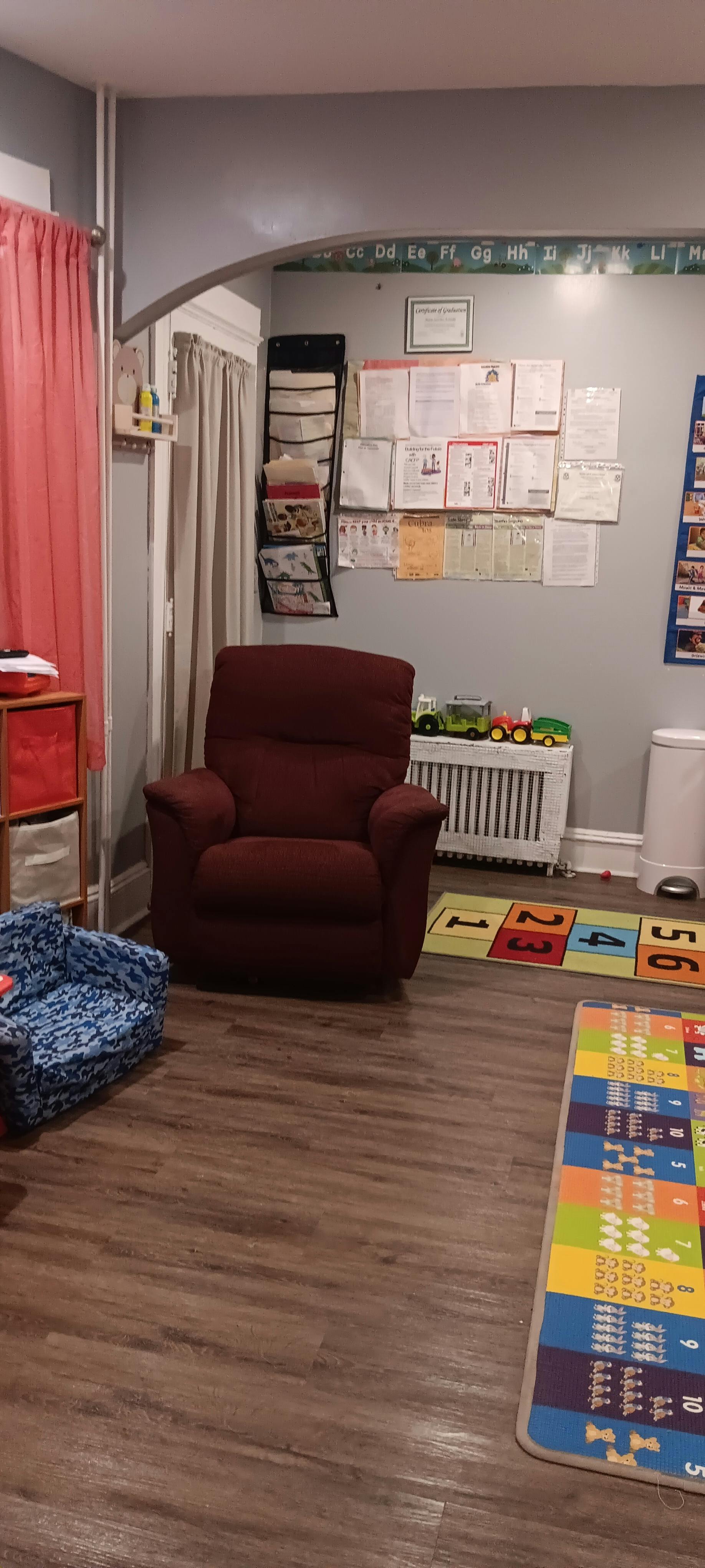 A room with a red armchair, a blue child's chair, and colorful rugs on a wood floor