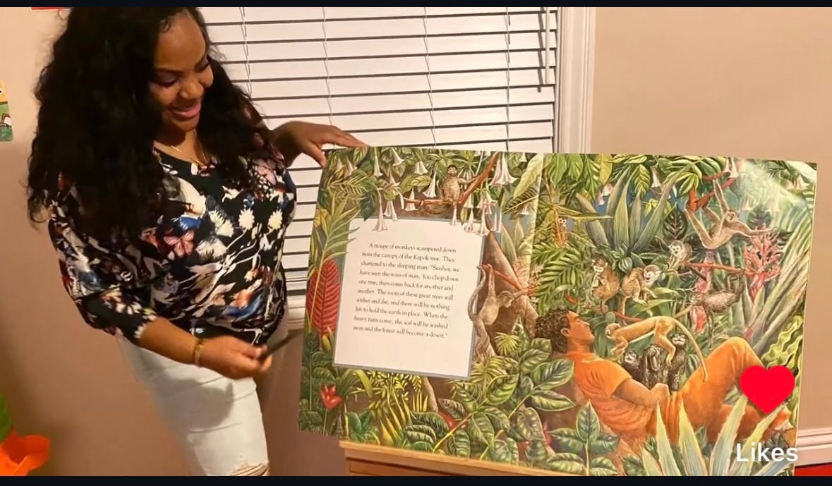Person holding up a large open book with an illustration of a jungle scene