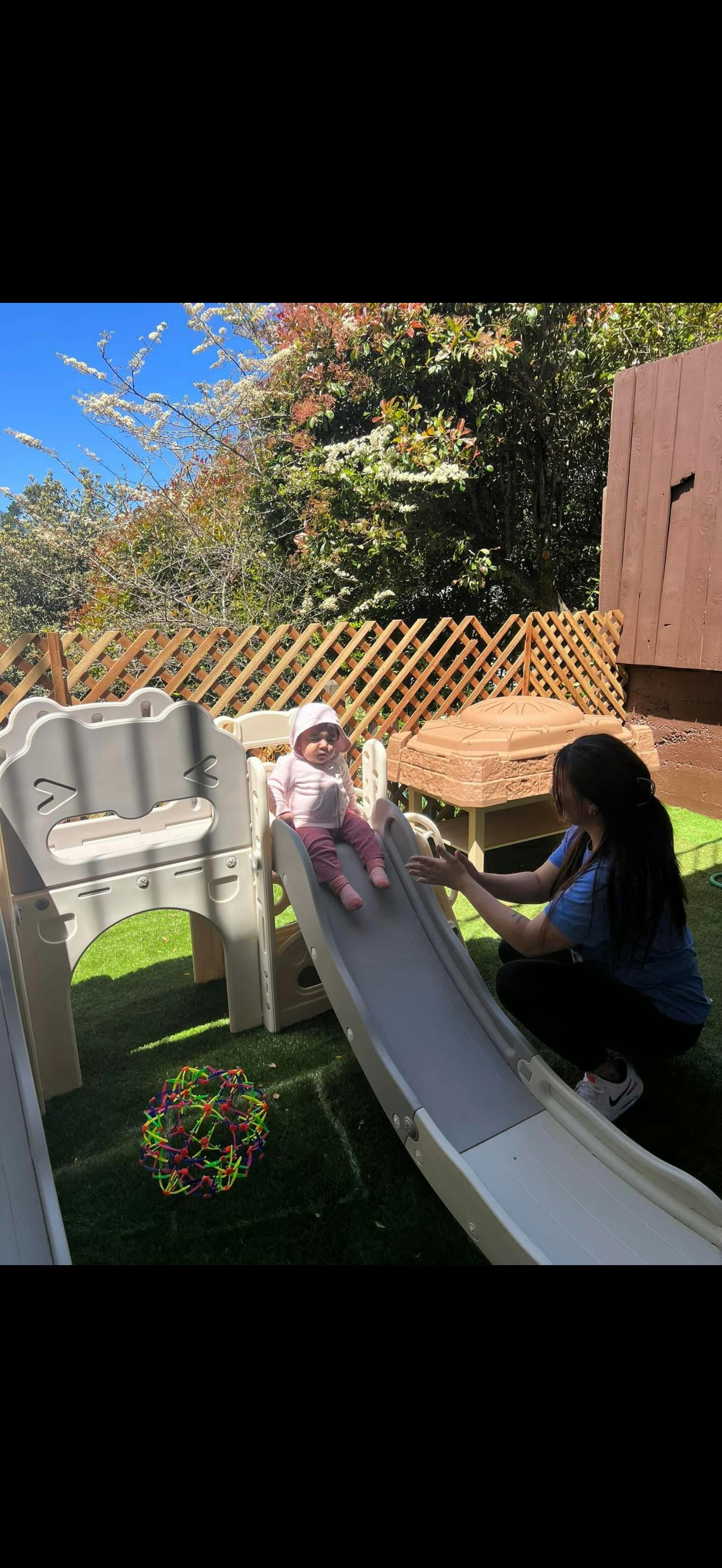 A person helping a child on a playground slide outdoors