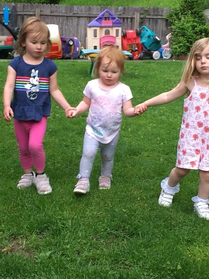 Three children holding hands and walking on grass
