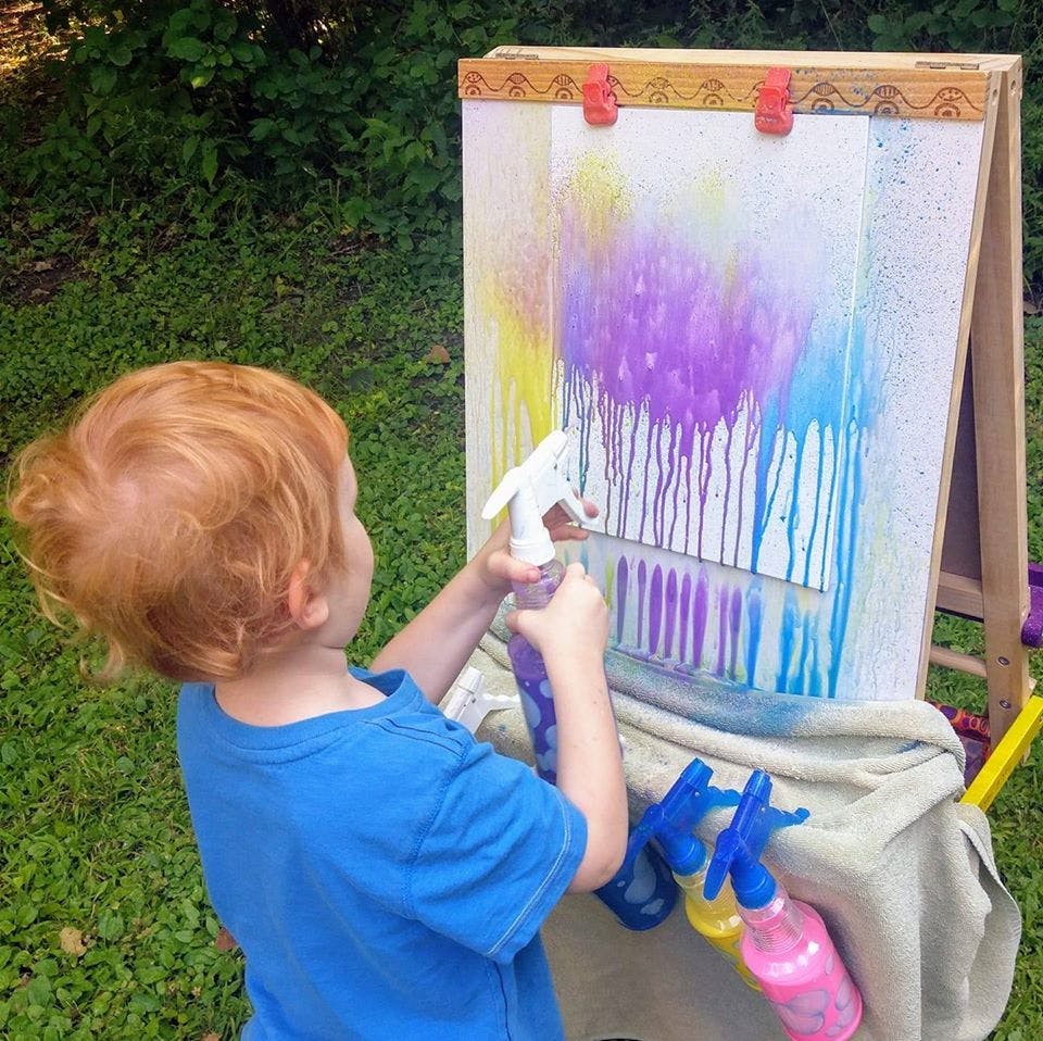 Child spraying paint onto an easel