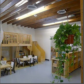 Indoor classroom with wooden loft, tables, and hanging plant