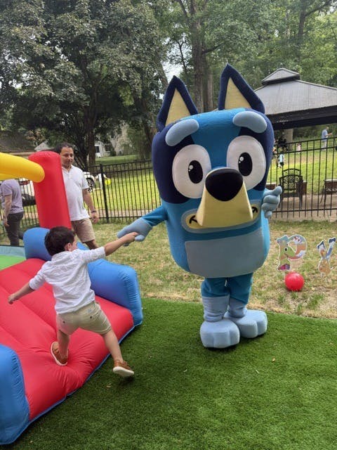 Child holding hands with a Bluey mascot character near an inflatable bounce house