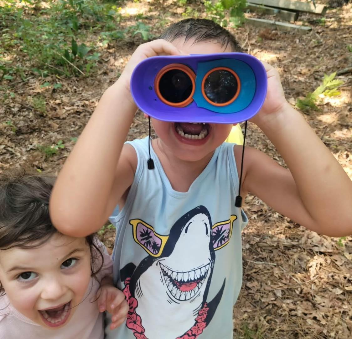 Child looking through toy binoculars, another child next to them