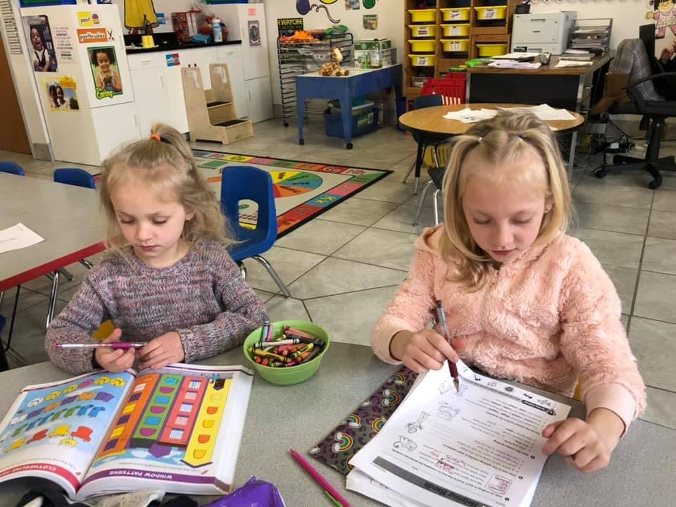 Two children sitting at a table with books and pencils in a classroom
