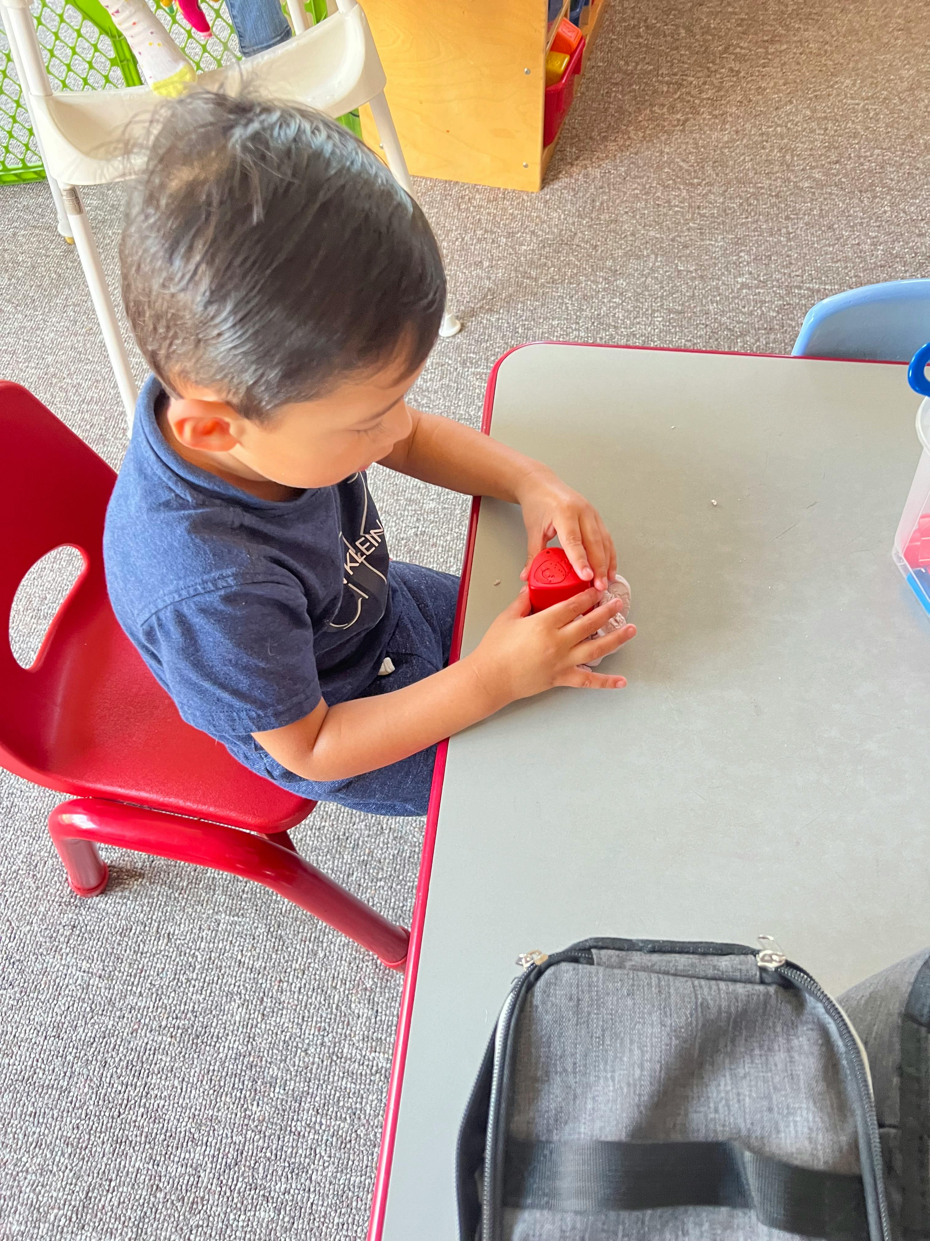 Child sitting at a table playing with a red block