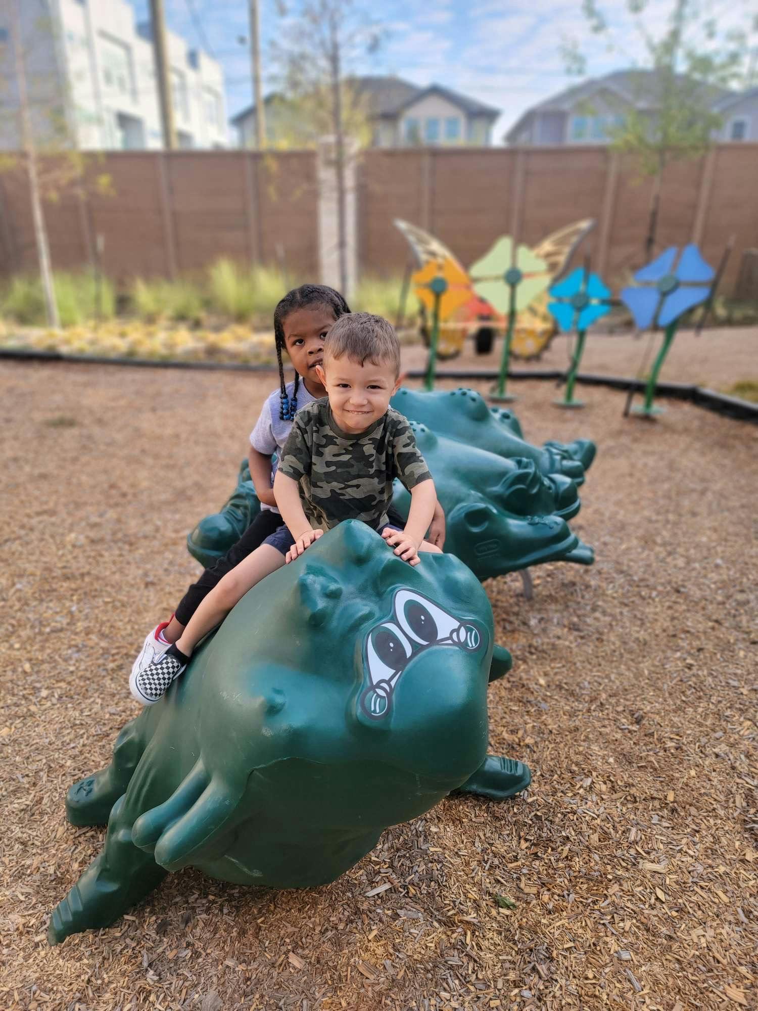 Two children on a green frog-shaped spring rider at a playground