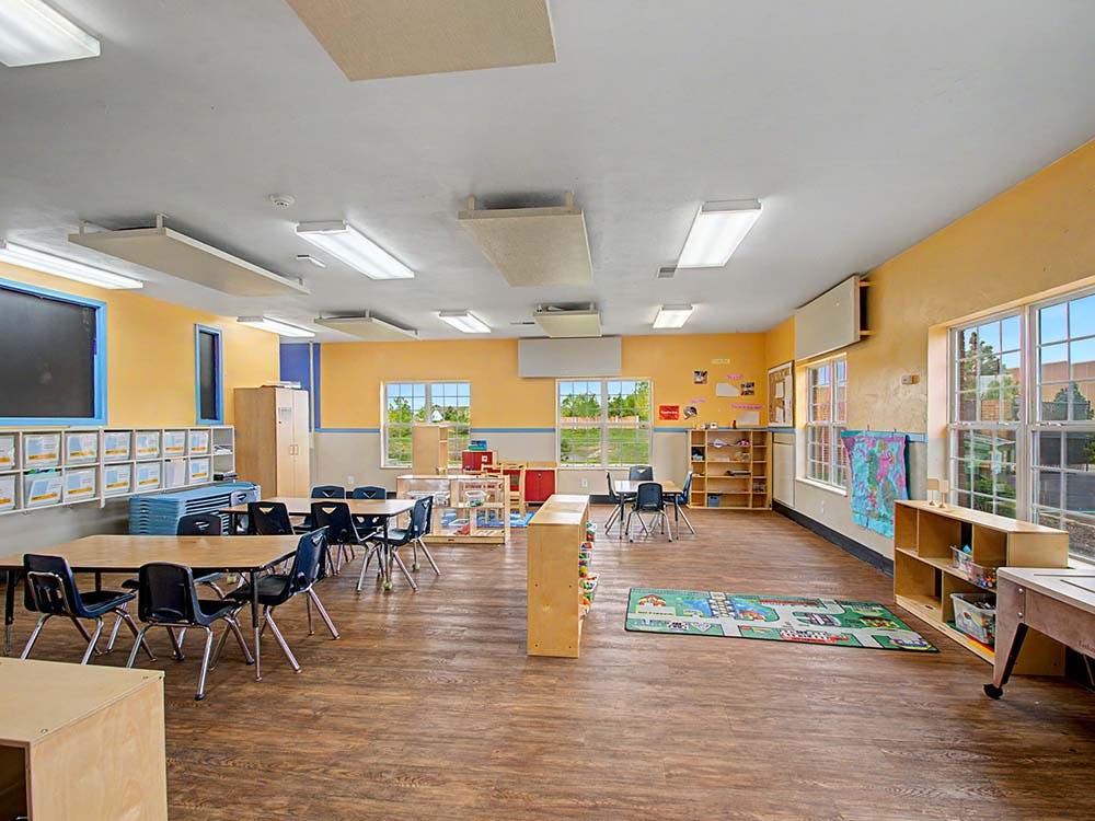 Empty classroom with tables, chairs, shelving units, and large windows