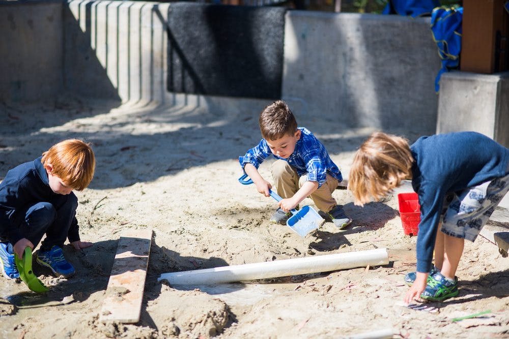 Three children playing in a sandbox with shovels and buckets