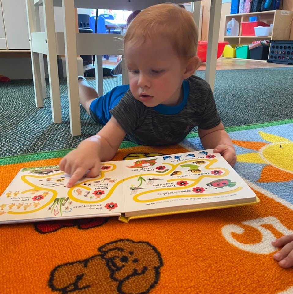 Child lying on floor pointing at an open book