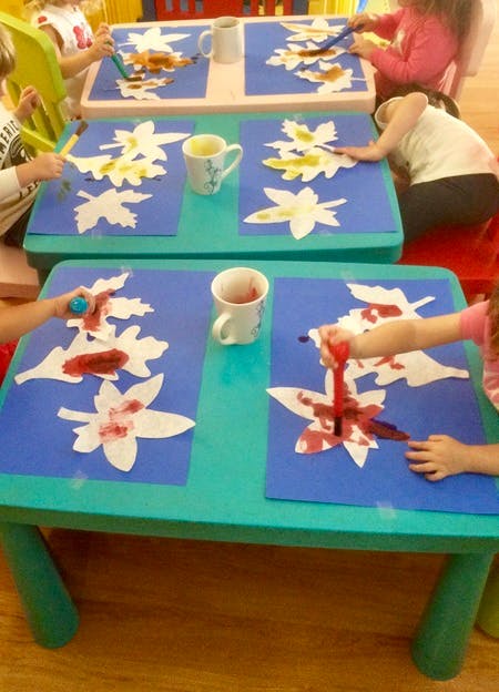 Children painting leaf cutouts at tables