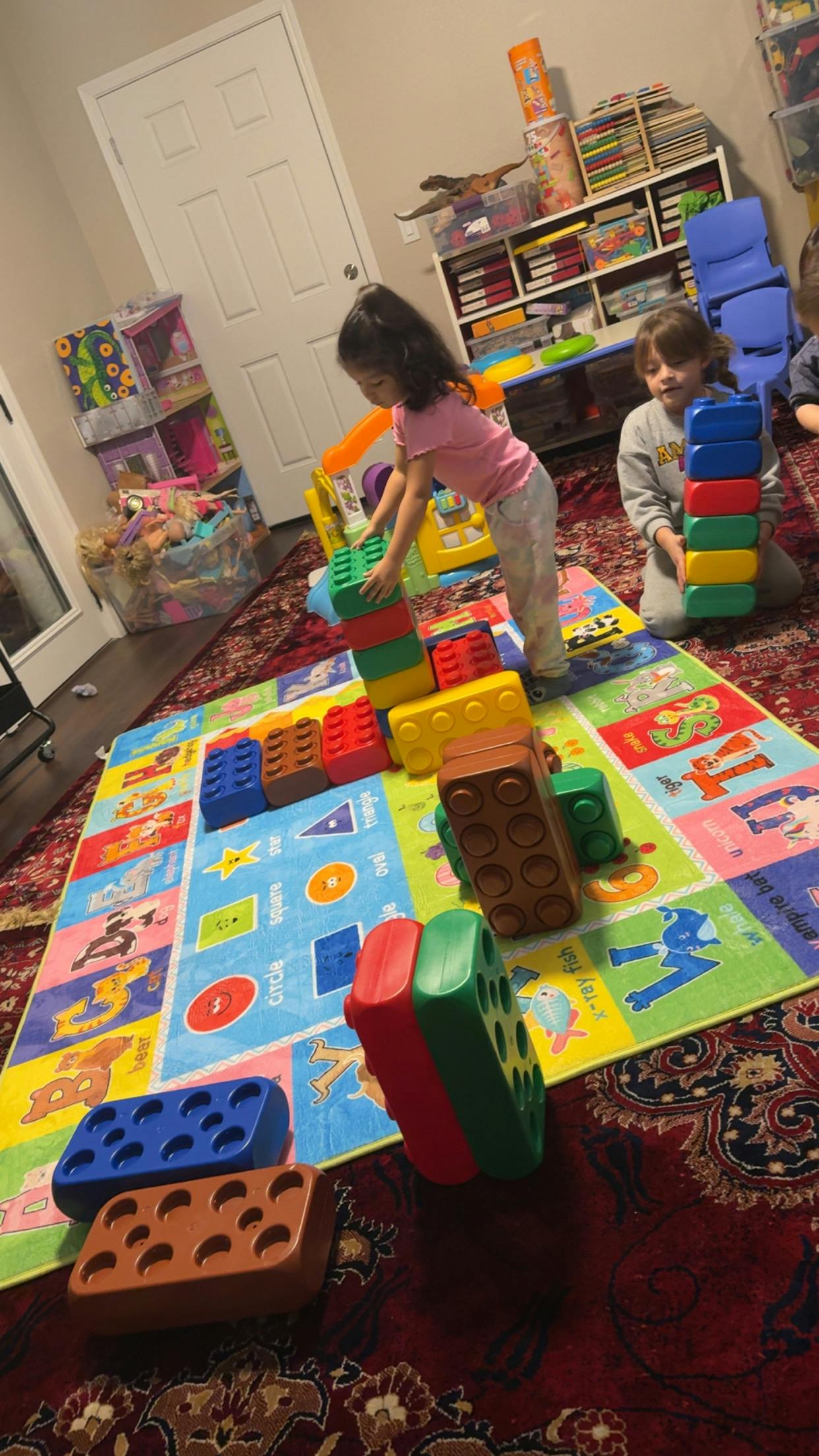 Two children playing with large colorful building blocks on a rug